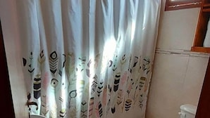 Une petite salle de bain avec deux toilettes, un lavabo et un rideau de douche orné d’un motif de feuilles.