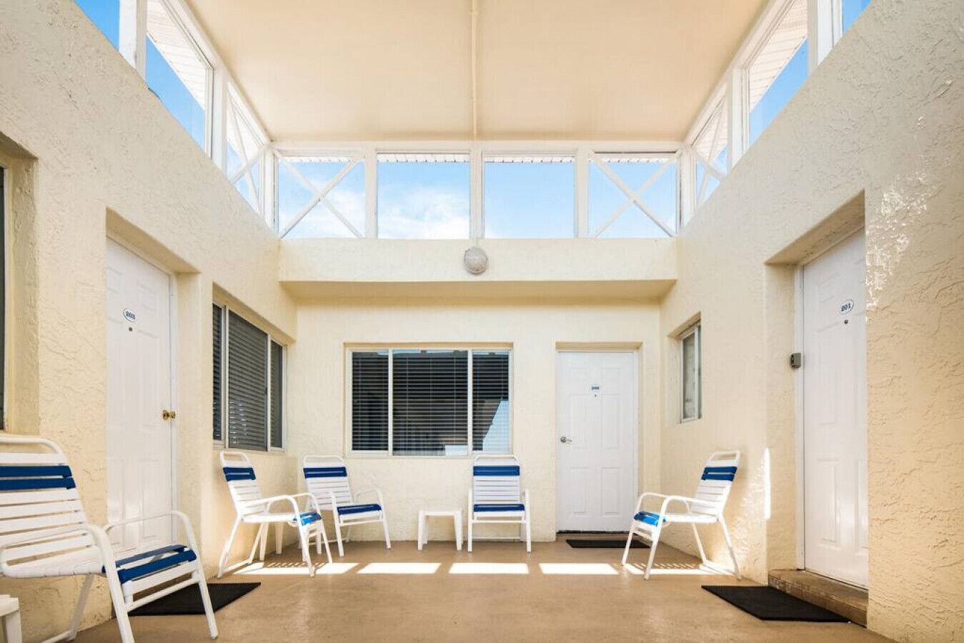 A covered outdoor seating area with white chairs and a central window.