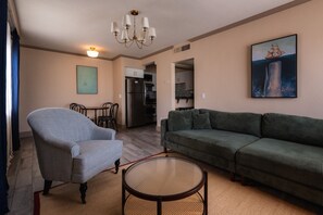 Ein Wohnzimmer mit einem gestreiften Sessel, einem grünen Sofa, einem runden Couchtisch und einem Gemälde eines Schiffes.