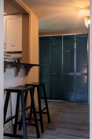 Quarto com cozinha compacta, sala de jantar com banquetas e conjunto de portas deslizantes escuras.