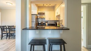 Una cocina compacta con una isla central, electrodomésticos de acero inoxidable y un comedor con dos taburetes.