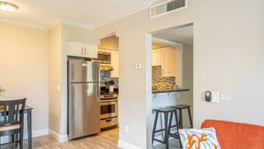 Cocina compacta con refrigerador, horno y una pequeña zona de comedor con mesa y sillas.
