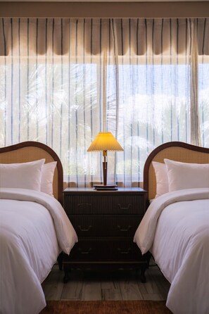 Ein Hotelzimmer mit zwei Betten, einem Nachttisch mit Lampe und einem Fenster mit Vorhängen.