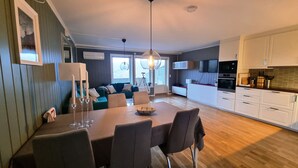 A modern kitchen with white cabinets, a dining area with a table and chairs, and a living area with a sofa and a TV. - Modern apartment with fantastic mountain and fjord  views! (Valestrandsfossen)