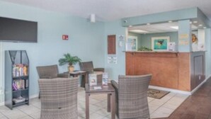 A reception area with a counter, seating, a bookshelf, and a door. - Turtle Reef Club Resort B (Jensen Beach)