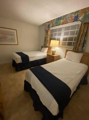 Two single beds with matching bedspreads are positioned against a floral wallpaper backdrop.