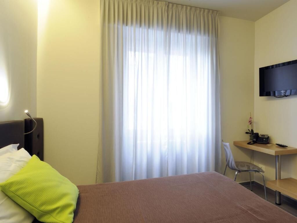Ein Hotelzimmer mit Bett, Schreibtisch, Stuhl, Fernseher und einem Fenster mit Vorhängen.