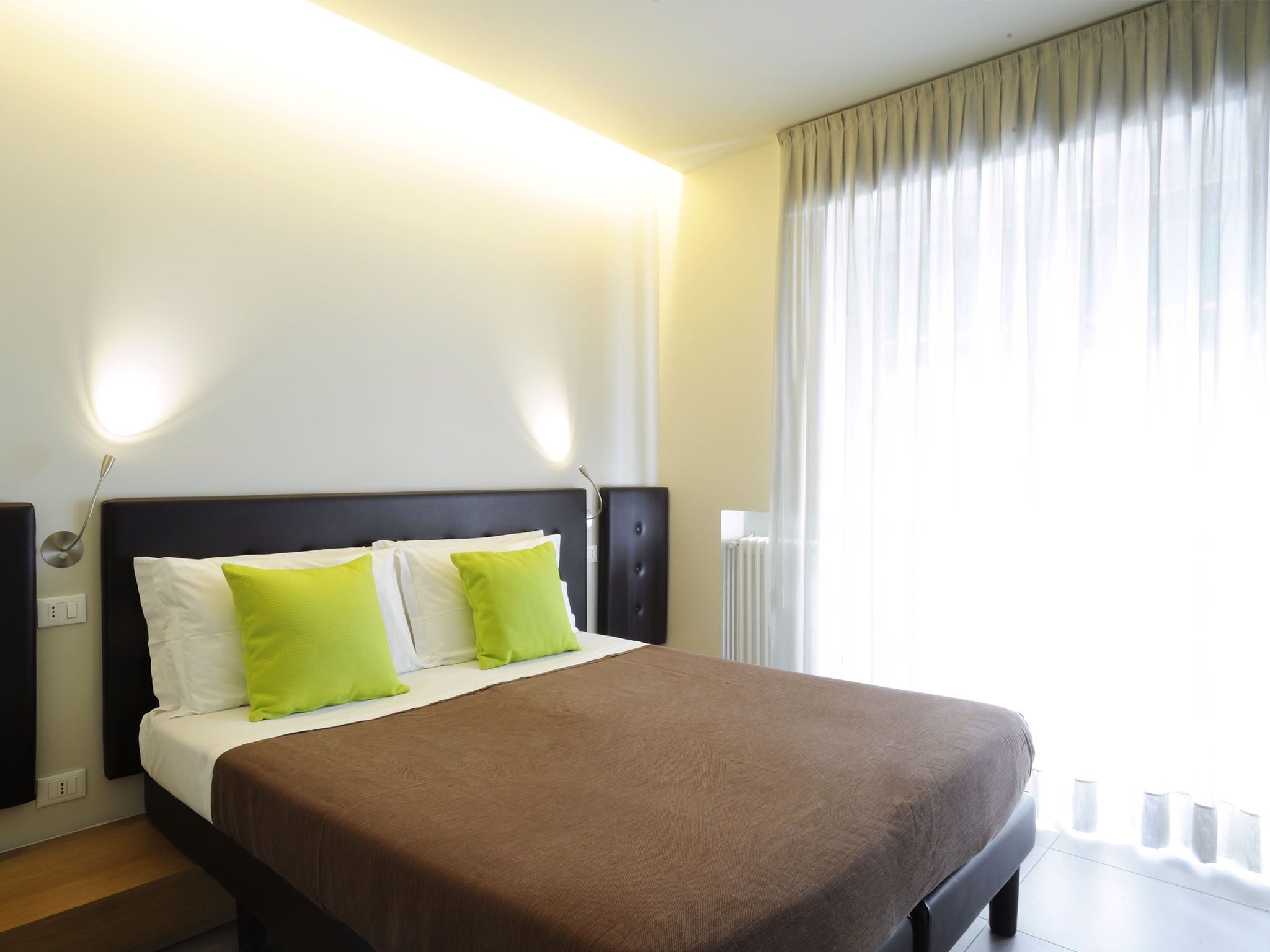 A hotel room with a large bed, two pillows, a nightstand, a lamp, and a window with curtains.