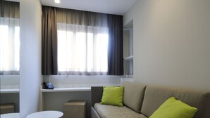 A modern living room with a sofa, two small tables, a window with curtains, and a built-in shelf. - Hotel Concordia (Loano)