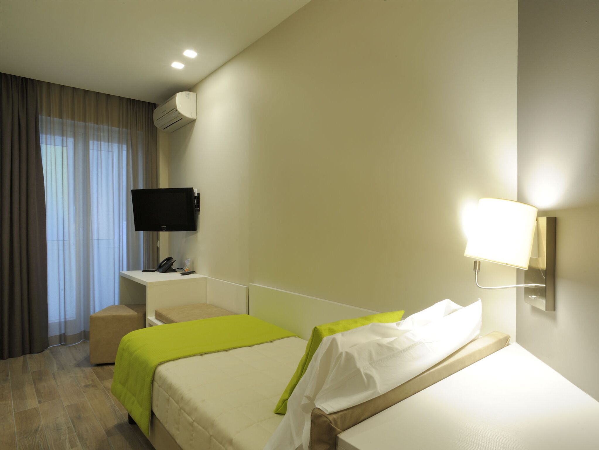 Ein Hotelzimmer mit Bett, Nachttisch, Fernseher und Wandlampe.