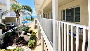 A hotel balcony with a pool view, a palm tree, and a staircase leading to another level. - Condo On The Beach - Heated Pool - Self Check-in (Belleair Beach)