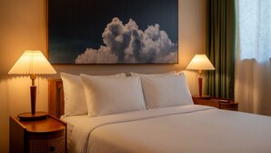 A hotel room with a bed, two bedside lamps, a painting of clouds, and a green curtain. - Condo On The Beach - Heated Pool - Self Check-in (Belleair Beach)