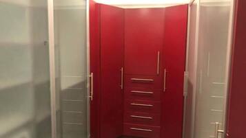 Un pasillo estrecho con un armario rojo que tiene varios cajones y una puerta de espejo.