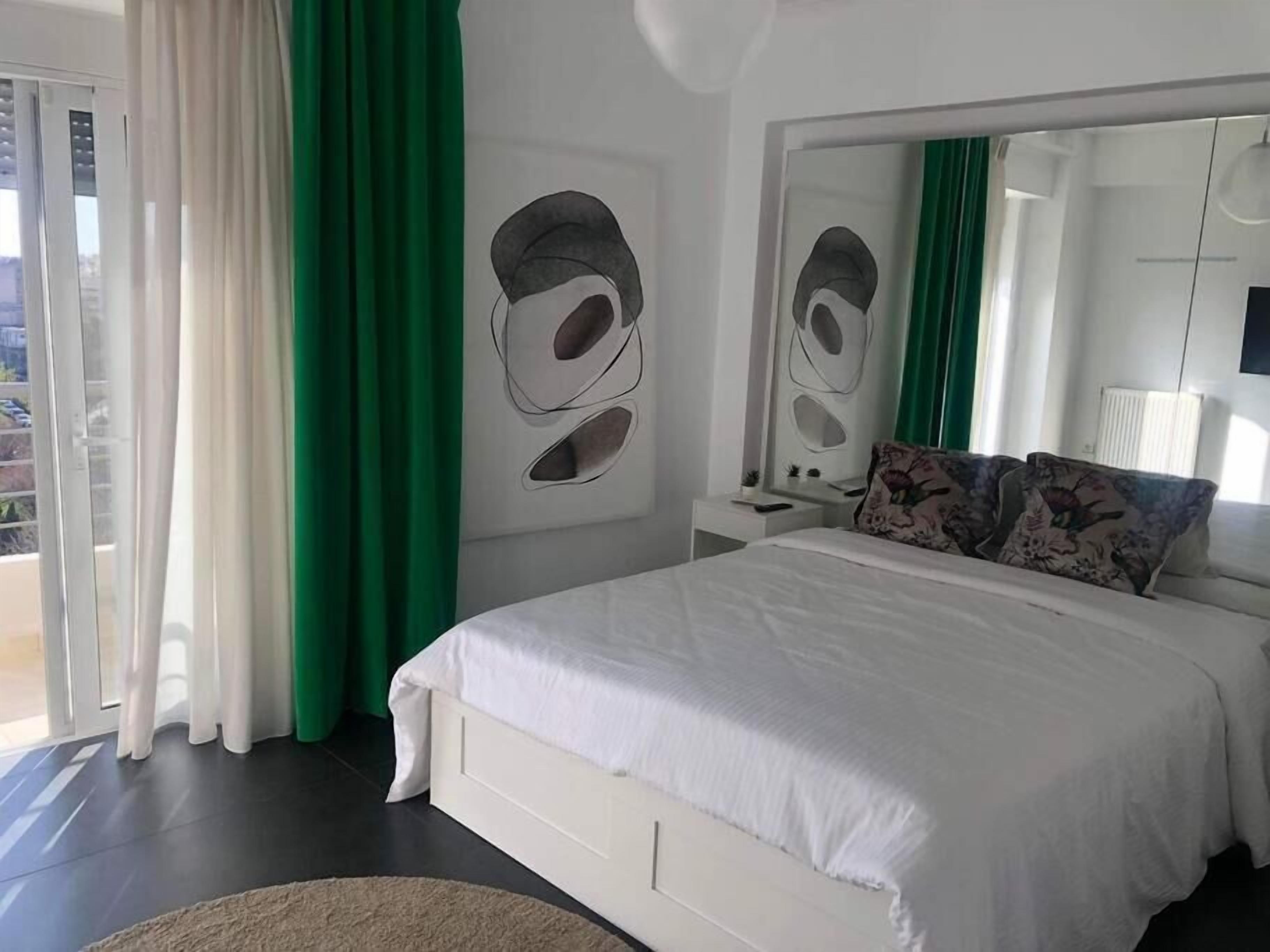Ein Schlafzimmer mit einem großen Bett, einem Nachttisch, einem Spiegel und Blick ins Freie.