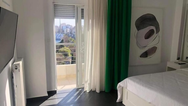 Un dormitori amb un llit, una televisió, una finestra amb cortines i vistes a la ciutat.