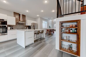 Une cuisine moderne avec des meubles blancs, un mur de fond en briques et un îlot central doté de tabourets de bar.