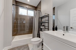 A modern bathroom with a bathtub, toilet, and vanity. - Modern 3BR Home w/ Backyard, BBQ grill & Sauna! (Austin)
