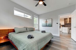 A bedroom with a bed, bedside tables, a ceiling fan, and a view into the kitchen. - Modern 3BR Home w/ Backyard, BBQ grill & Sauna! (Austin)