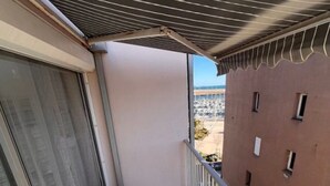 Uma varanda com grade de metal, vista para um parque de estacionamento e um edifício ao fundo.