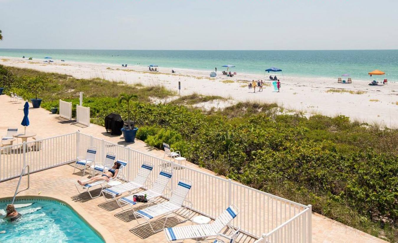 A pool area with lounge chairs and a view of the beach.