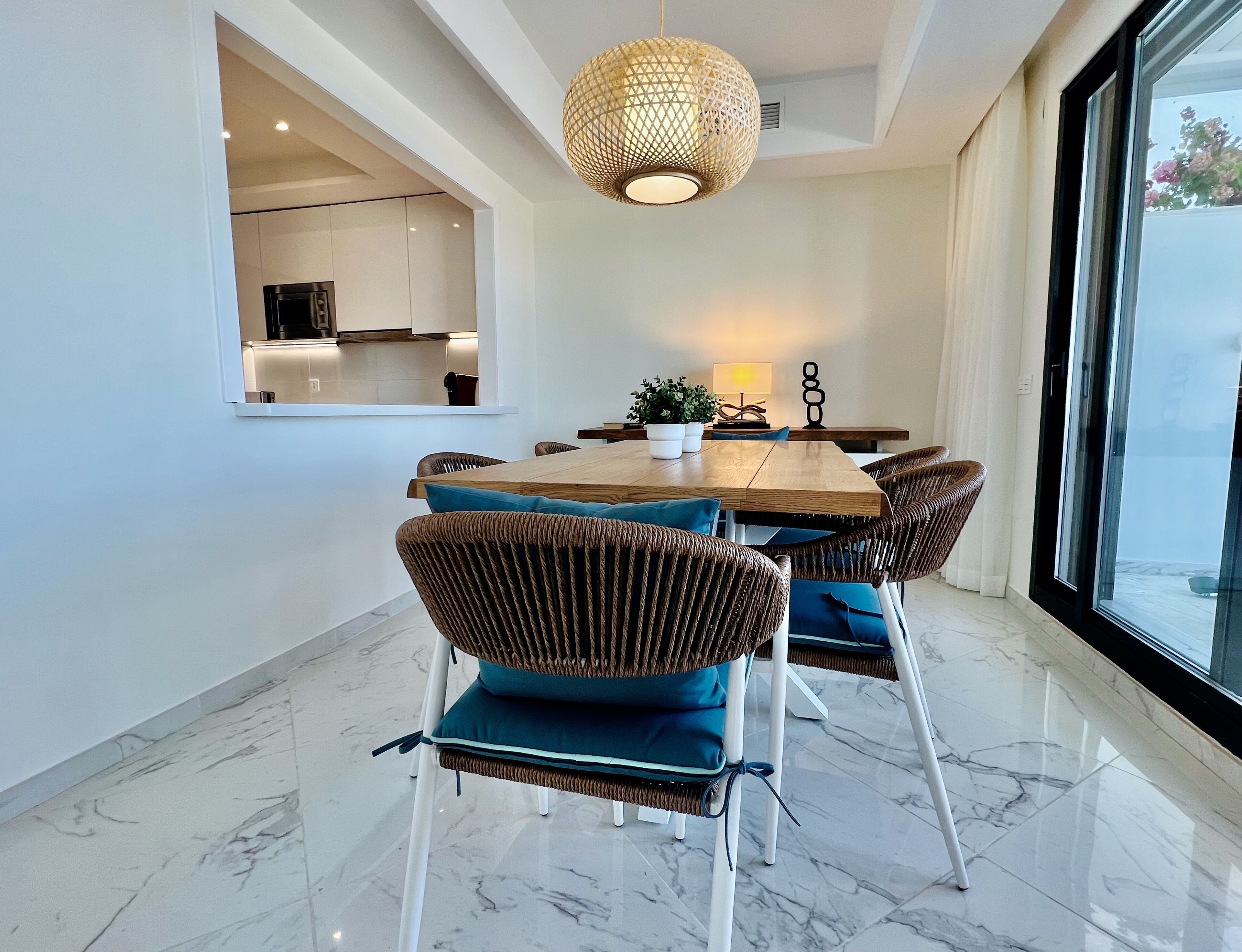 Un comedor moderno con una mesa de madera, sillas de mimbre con cojines azules y una lámpara colgante.