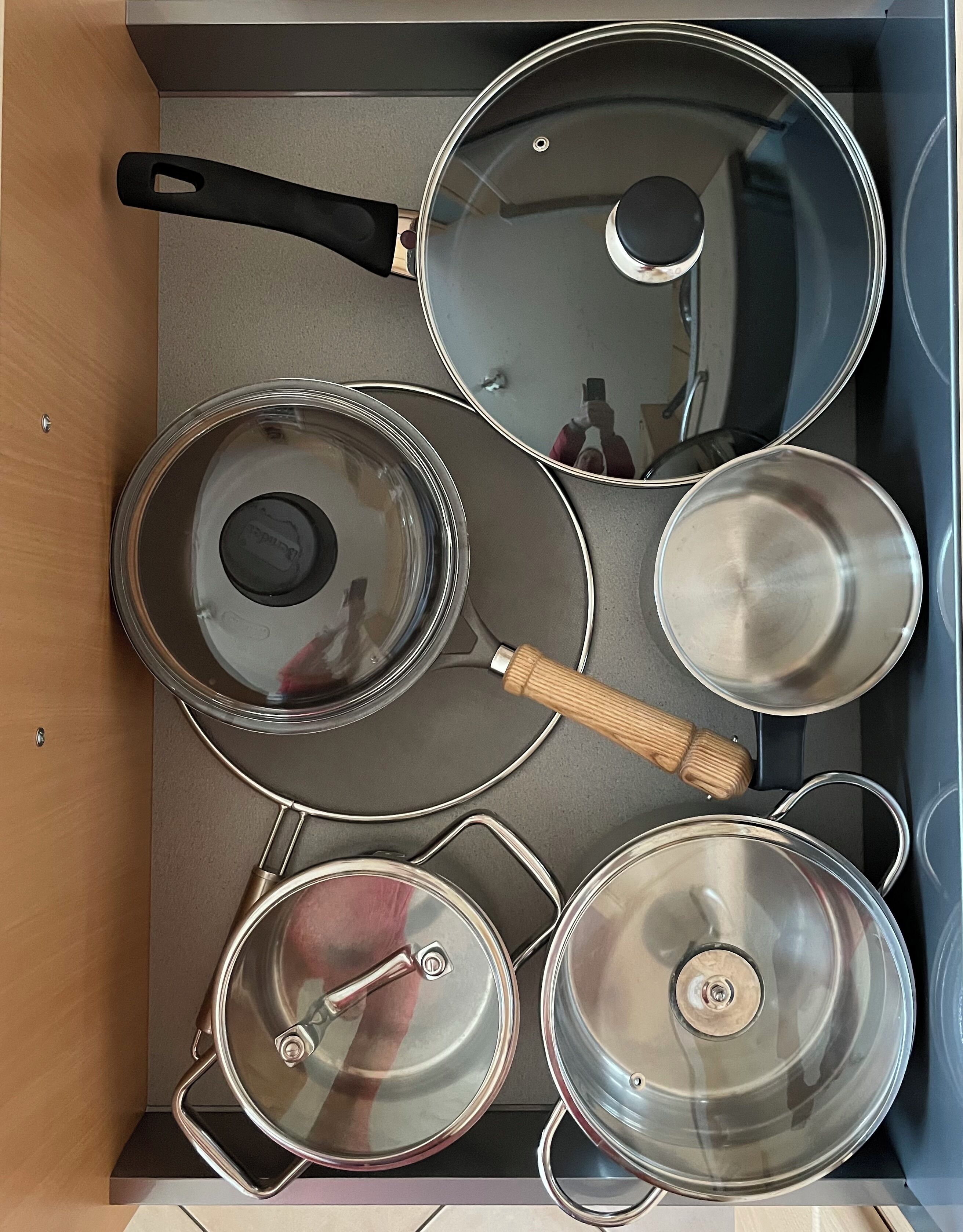 A kitchen drawer with various pots and pans, including a frying pan, a saucepan, and a pot with a wooden handle.
