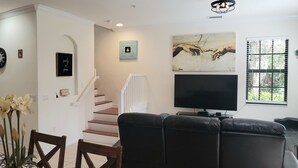 Una cocina moderna con refrigerador, estufa y armarios de madera. Hay un comedor con mesa y sillas, y una sala de estar con sofá y televisor.