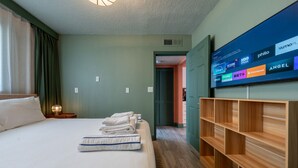 A hotel room with a bed, a TV mounted on the wall, and a wooden shelf unit. - Condo On The Beach - Heated Pool - Self Check-in (Belleair Beach)