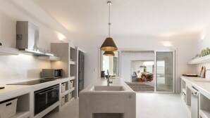 A modern kitchen with built-in appliances, a central island, and a view to the dining area. - Aura villa A story to tell  (Mykonos)