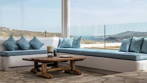A modern outdoor seating area with a sofa and a wooden table, overlooking a scenic landscape. - Aura villa A story to tell  (Mykonos)