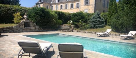 A pool area with lounge chairs and a stone building in the background.