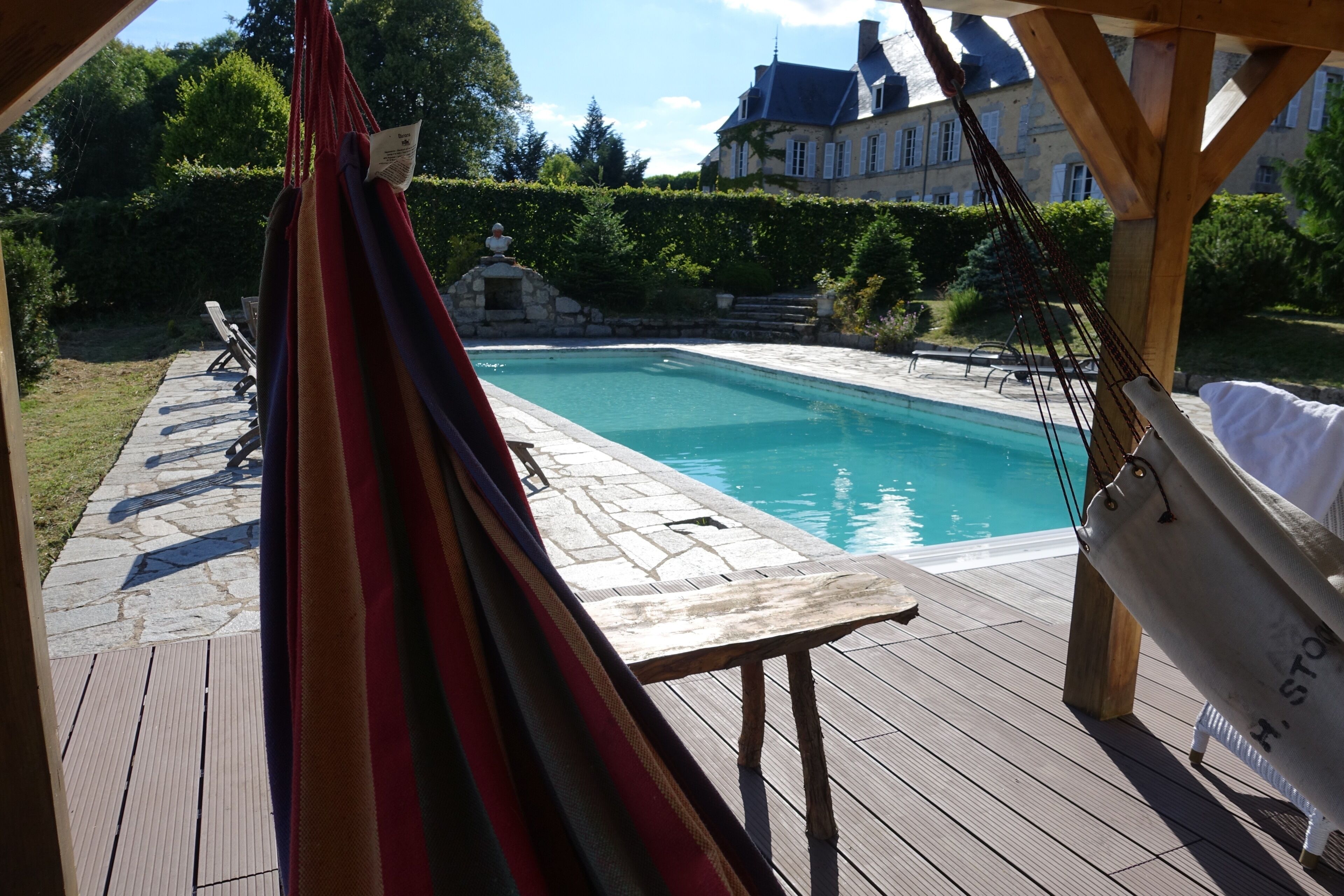 Un terrazzo in legno con piscina, un'amaca e vista su una grande casa sullo sfondo.