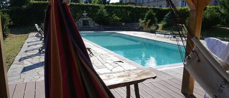 Un terrazzo in legno con piscina, un'amaca e vista su una grande casa sullo sfondo.