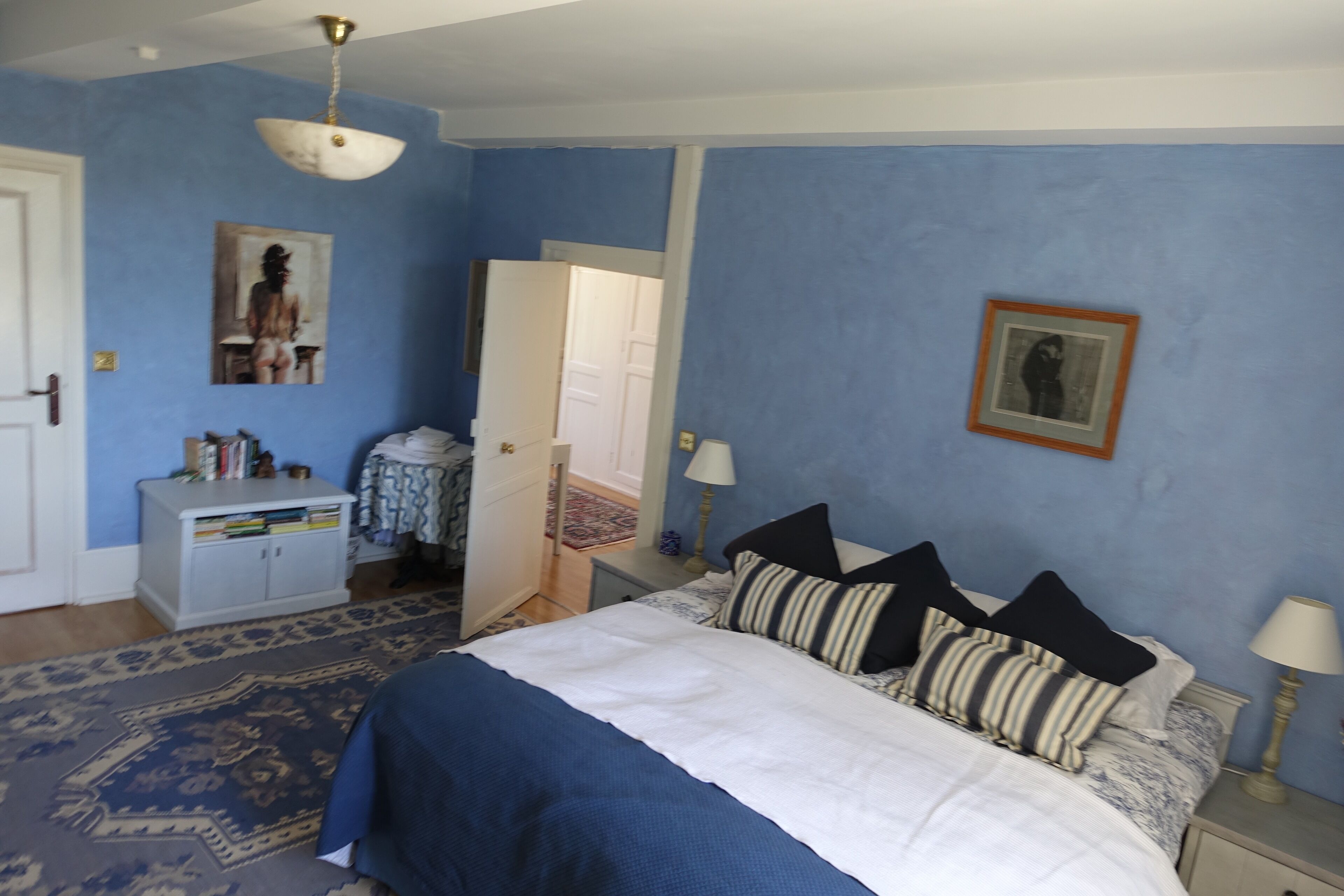 A bedroom with a bed, bedside tables, a wardrobe, and a door leading to another room.