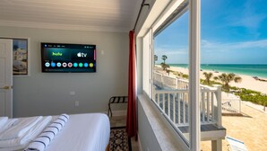 Een hotelkamer met een bed, een televisie waarop Hulu en Apple TV worden getoond, en een balkon met uitzicht op het strand.