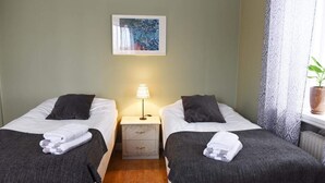 Habitación doble con dos camas, una mesita de noche con lámpara, un cuadro en la pared y una ventana con cortinas.