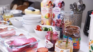 Una encimera de cocina con diversos alimentos, entre ellos frascos de mermelada, un tazón de ensalada y recipientes con carne.