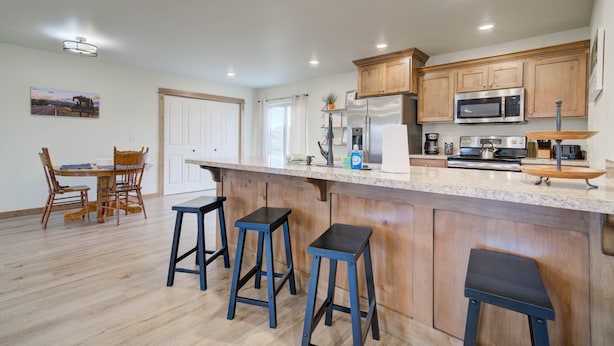 Una cocina moderna con armarios de madera, una isla central con taburetes, un comedor con mesa y sillas, y un refrigerador.