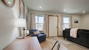 Una habitación con suelo de madera, un sillón azul, un sofá gris, una mesa de madera y una puerta con ventana.