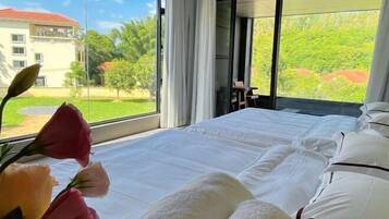 A bedroom with a large bed, a view of greenery outside, and a window with curtains.