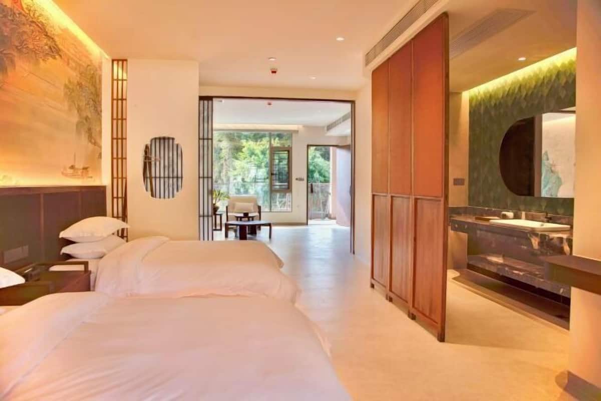 A hotel room with two beds, a bathroom with a large mirror, and a view of the outdoors.