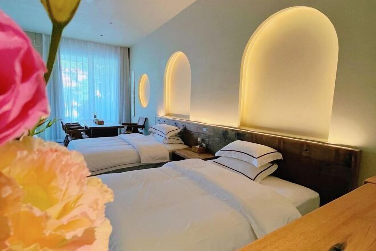 A hotel room with two beds, a wooden nightstand, a desk, and a chair.
