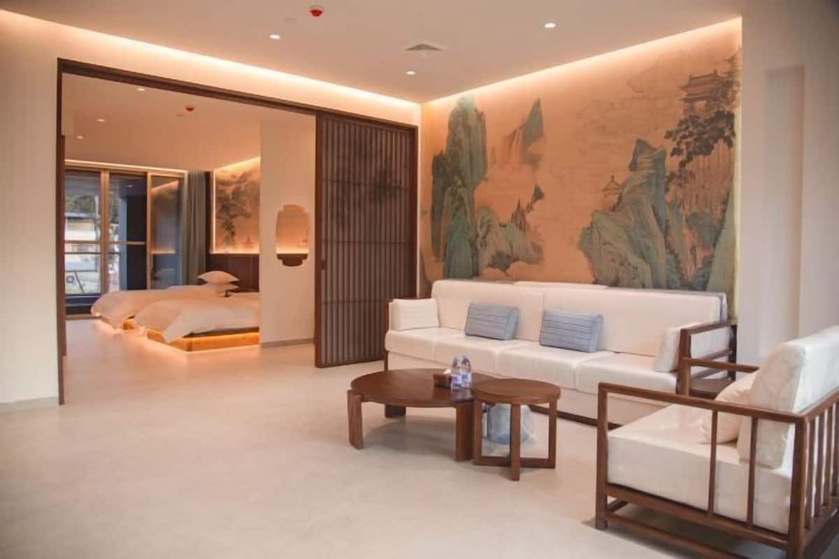 A modern hotel room with a bed, a white sofa, a wooden coffee table, and a large painting on the wall.