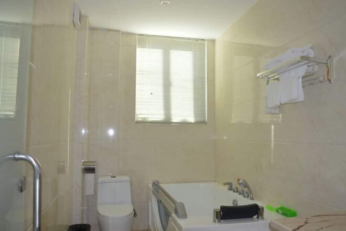 A bathroom with a bathtub, toilet, and a window with blinds.