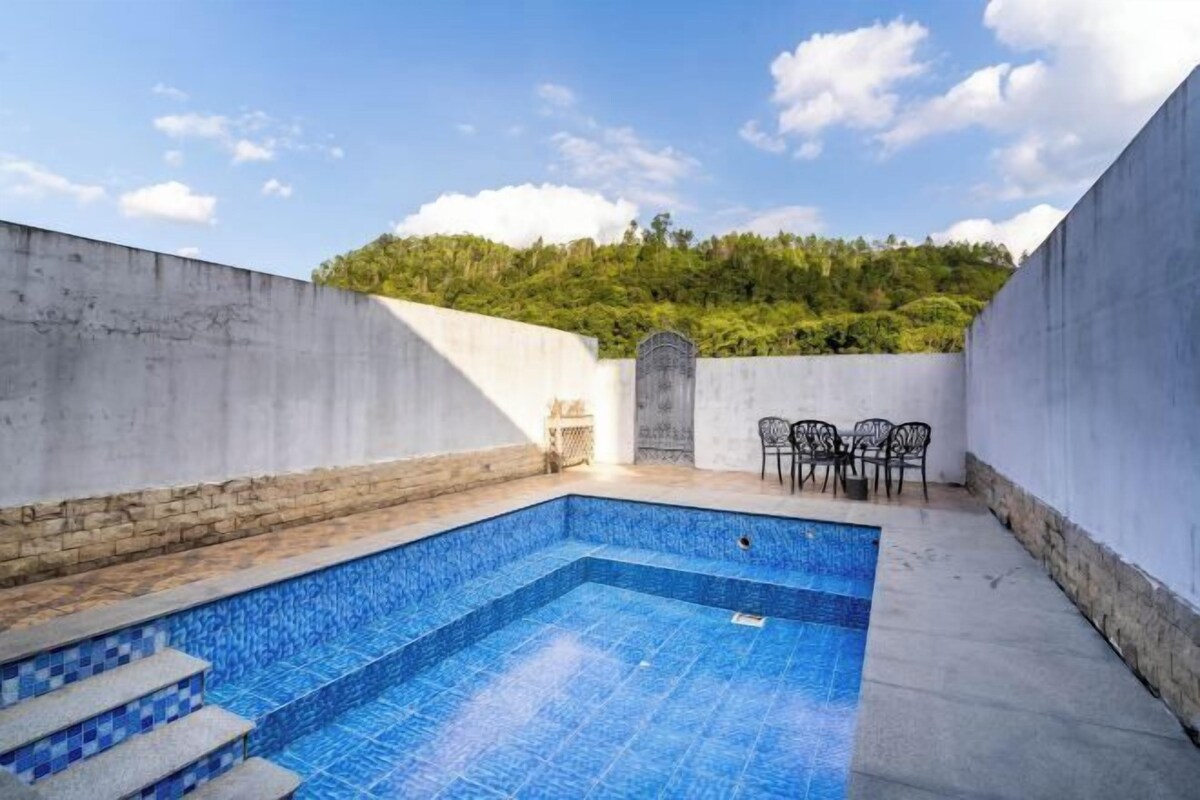 A swimming pool with steps leading into it, surrounded by walls and a small seating area with chairs.