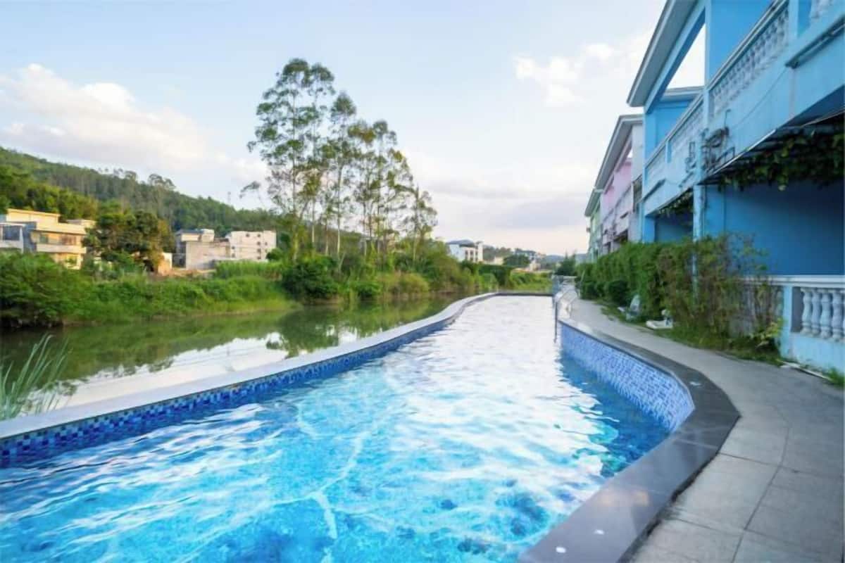 A swimming pool with a tiled edge, surrounded by greenery and buildings.