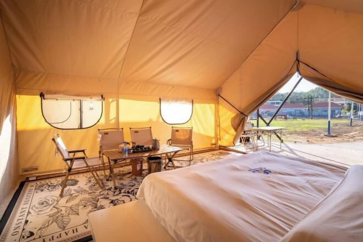 A tent with a bed, two chairs, a table, and a window.