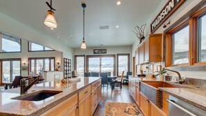 A spacious kitchen with wooden cabinets, a large island with a sink, and a view of mountains through large windows. - Madison River House - Ennis, MT (Madison County)