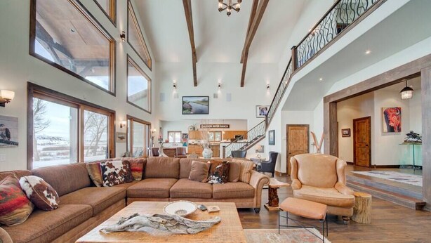 A spacious living room with a large sectional sofa, a wooden coffee table, and a staircase leading to an upper level. - Madison River House - Ennis, MT (Madison County)