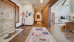 A spacious hallway with wooden flooring, a patterned rug, and a wooden wall with a mounted sign. - Madison River House - Ennis, MT (Madison County)